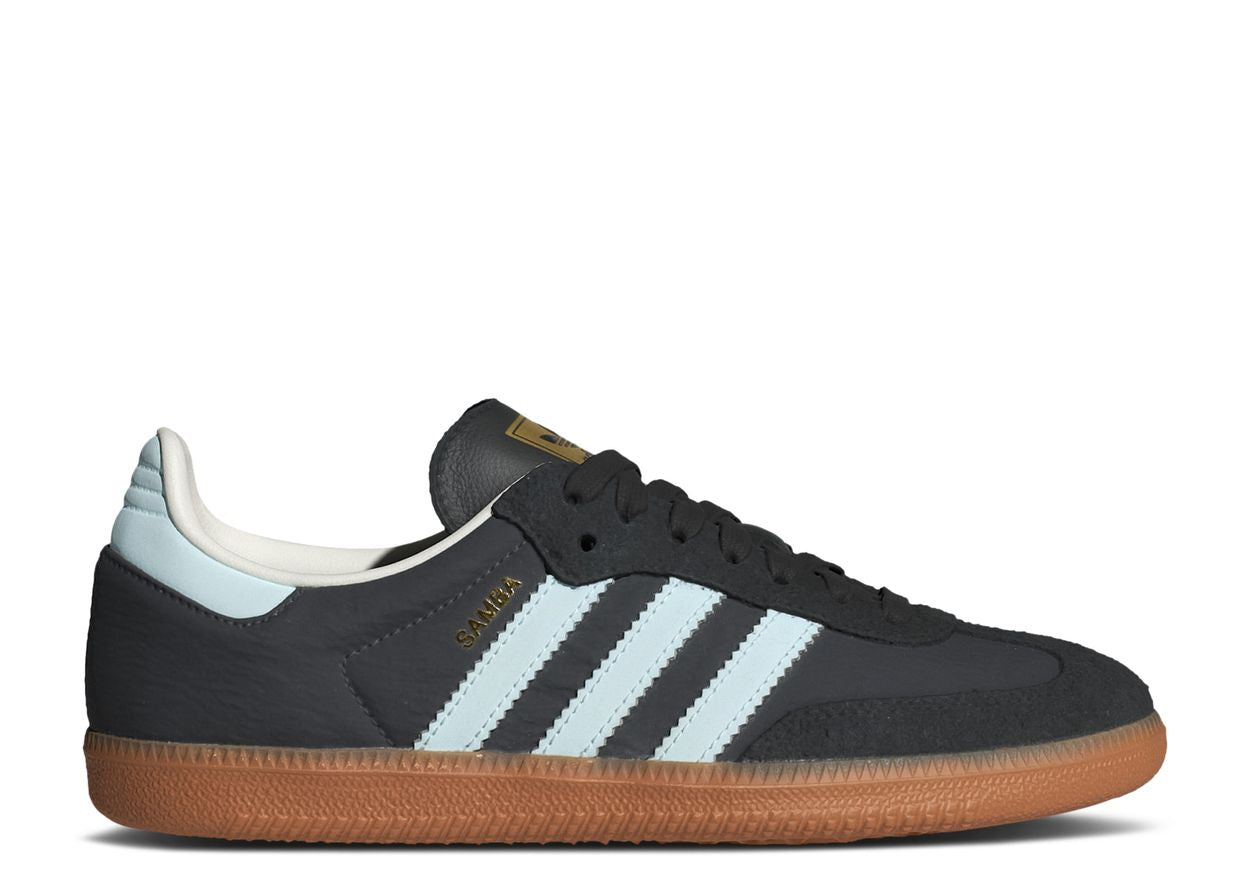 Adidas Samba OG Carbon W: A black sneaker with light blue stripes and heel tab, gum sole, white inner lining, and gold SAMBA text on the side is displayed against a white background.