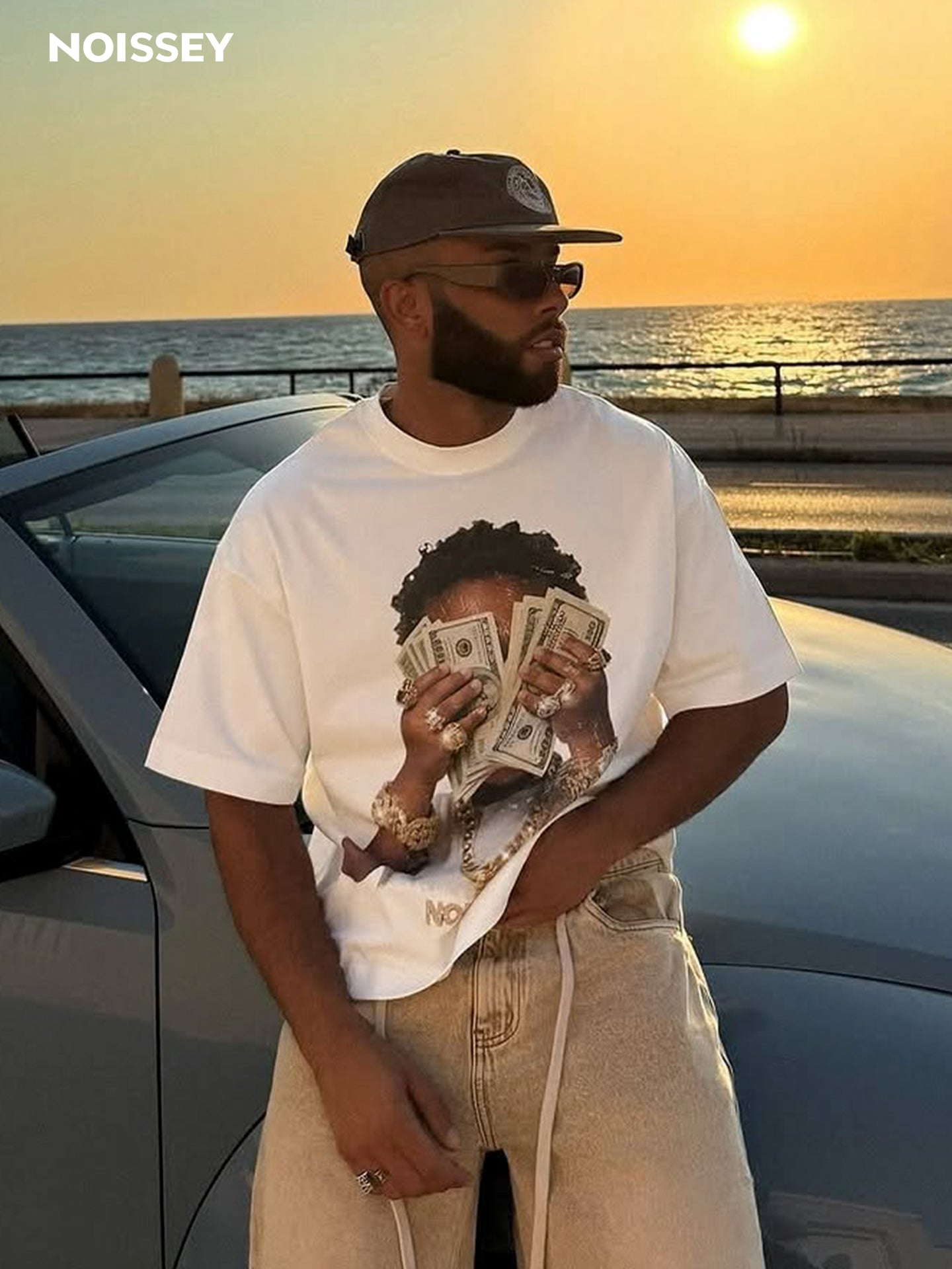 Male model wearing NOISSEY rich kid tee styled with baggy jeans at sunset